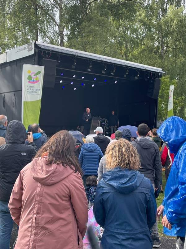 Quartiersfest Fischbeker Heidbrook für die IBA Hamburg 2022. Blick auf eine Bühne. Im Vordergrund Menschen mit Jacken bei Regen.
