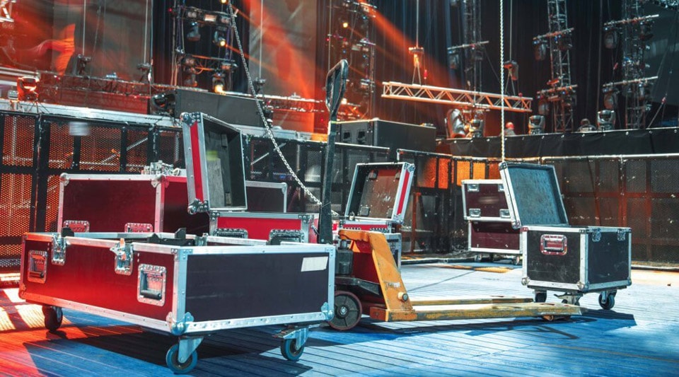 Equipment boxes are placed on the stage floor, which can be used for setting up and dismantling the event technology. Lighting systems and stage structures are illuminated by skylights, which illustrate the preparation process for a concert or show.