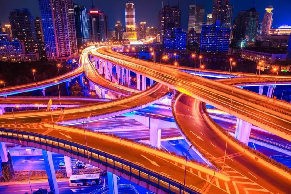 A complex network of highways is being illuminated at night with colorful lights. The roads and bridges are being depicted in vibrant blue and orange hues to create a lively cityscape.