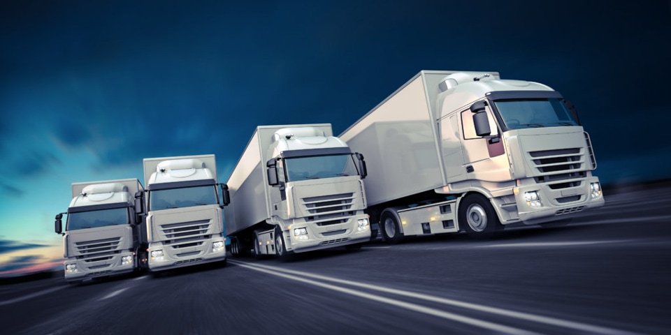 Several trucks are being shown side by side on a highway as they drive at dusk. The vehicles are being depicted in a dynamic formation to convey speed and power.