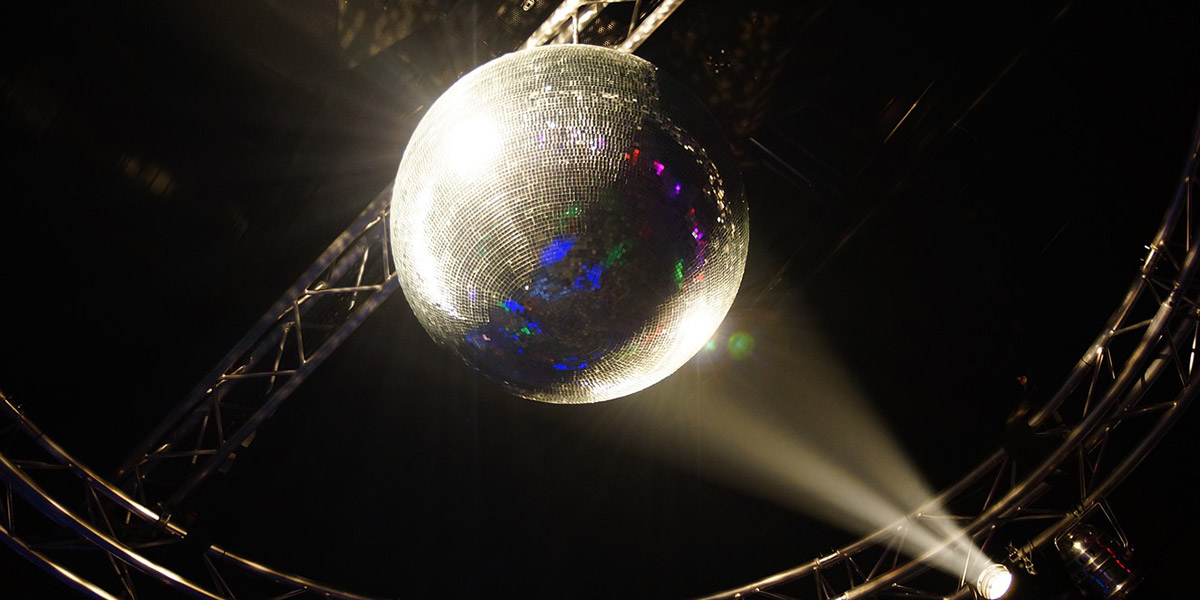 Successful event planning with SES. A large disco ball hangs in front of a dark background and is illuminated by bright spotlights.