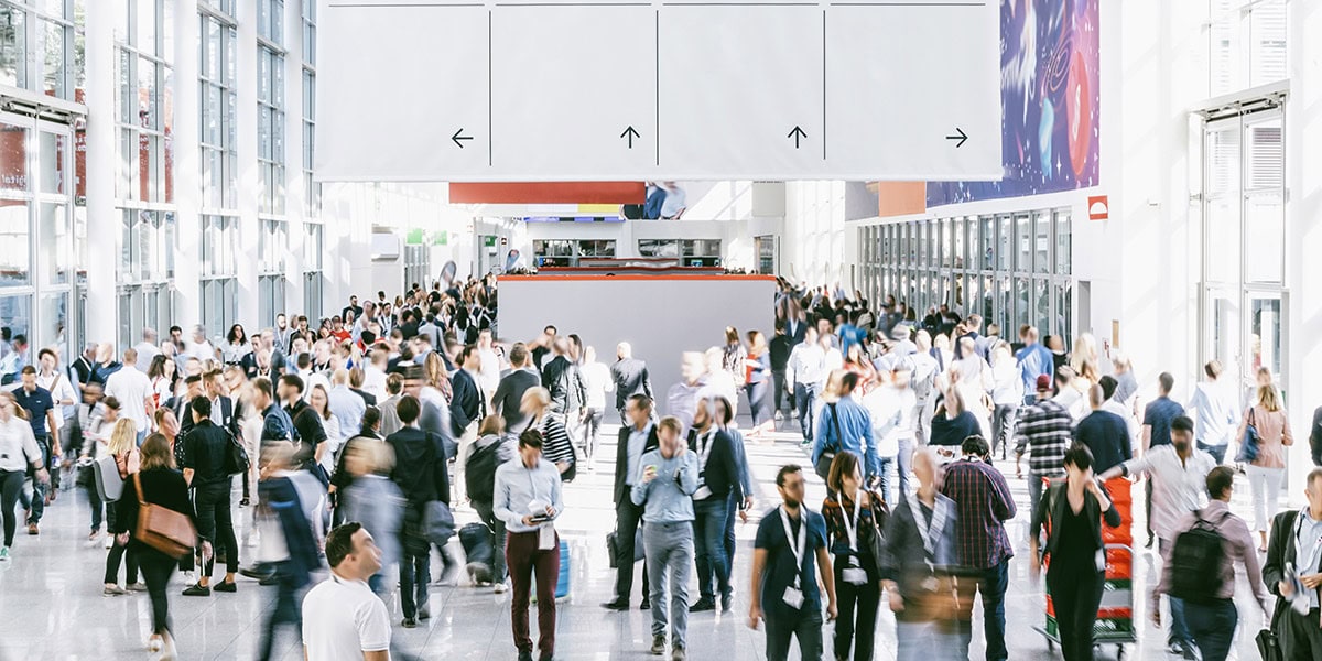 Trade show organization for organizers with SES. People walk down the aisle of an exhibition hall. Many of them are blurred.